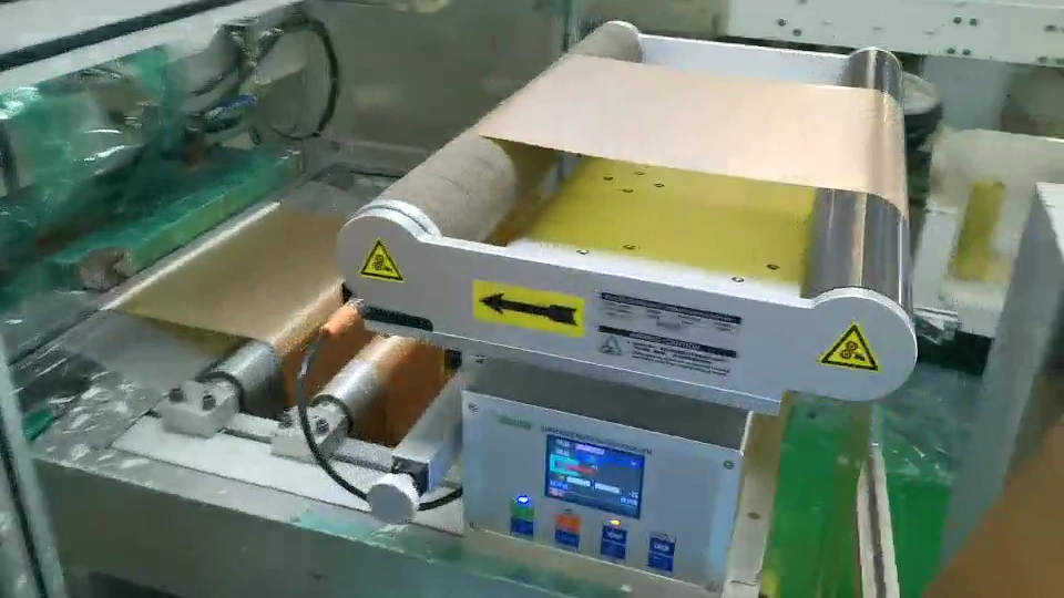 Bronze-coloured patterned web passing through a compact guide assembly with a controller mounted beneath the rollers