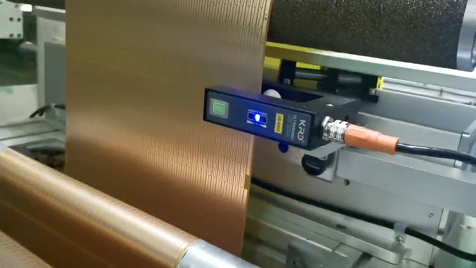 KRD ultrasonic edge sensor beside the edge of a bronze-coloured patterned web